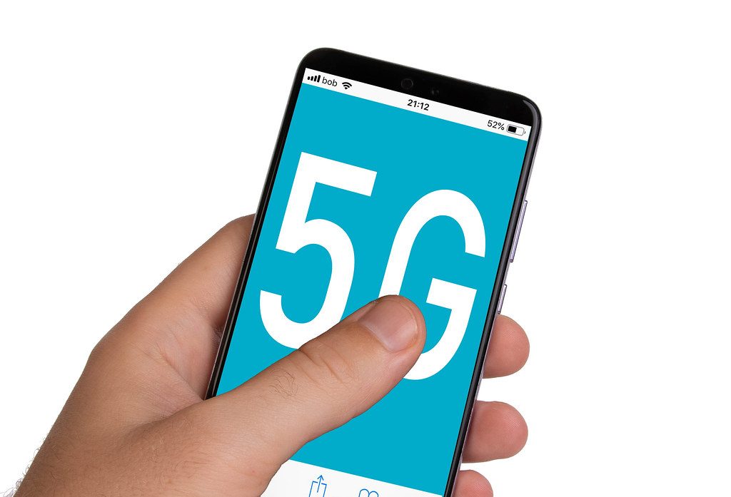 Manos masculinas sosteniendo un teléfono inteligente con texto 5G en la pantalla azul